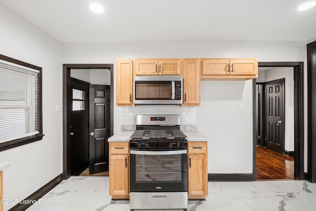 kitchen with marble finish floor, baseboards, appliances with stainless steel finishes, and backsplash