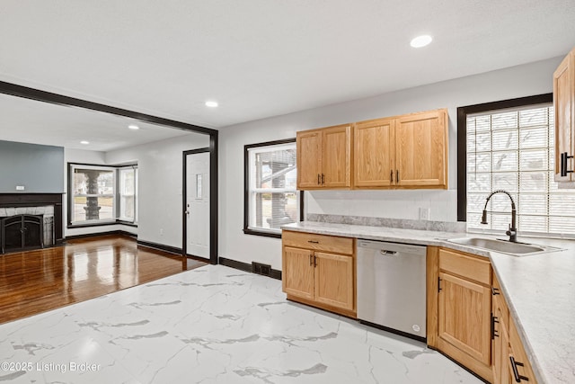 kitchen featuring a fireplace with flush hearth, light countertops, stainless steel dishwasher, and a sink