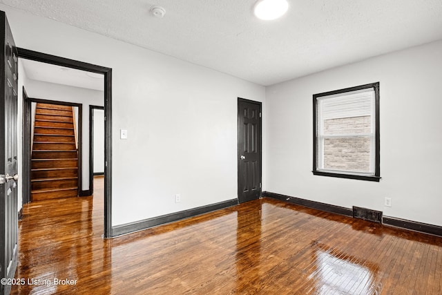 spare room featuring a textured ceiling, visible vents, baseboards, stairs, and wood-type flooring