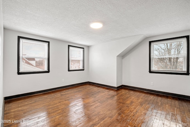 bonus room with dark wood-style flooring, a textured ceiling, and baseboards