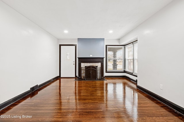 unfurnished living room featuring baseboards, a fireplace with flush hearth, visible vents, and wood finished floors