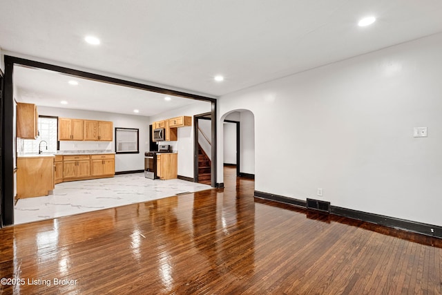 unfurnished living room with arched walkways, light wood-style floors, visible vents, and baseboards