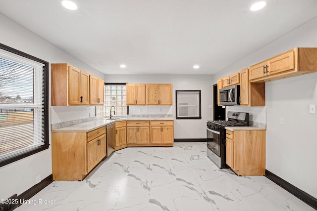 kitchen featuring stainless steel appliances, light countertops, a sink, and baseboards