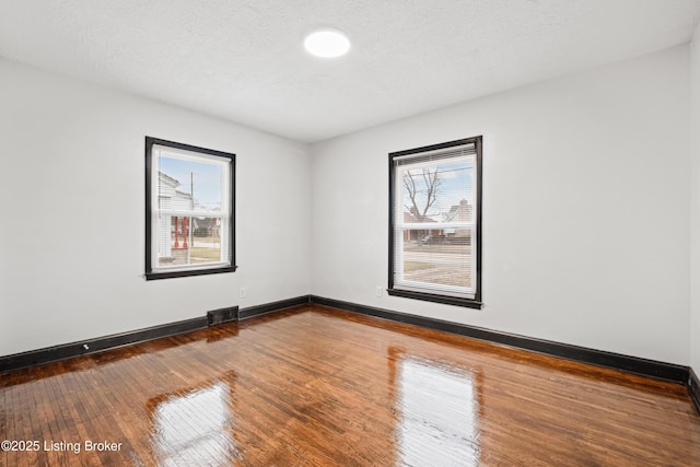 spare room featuring dark wood-style floors, a textured ceiling, visible vents, and baseboards