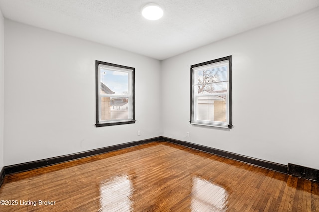 empty room with a textured ceiling, wood-type flooring, and baseboards