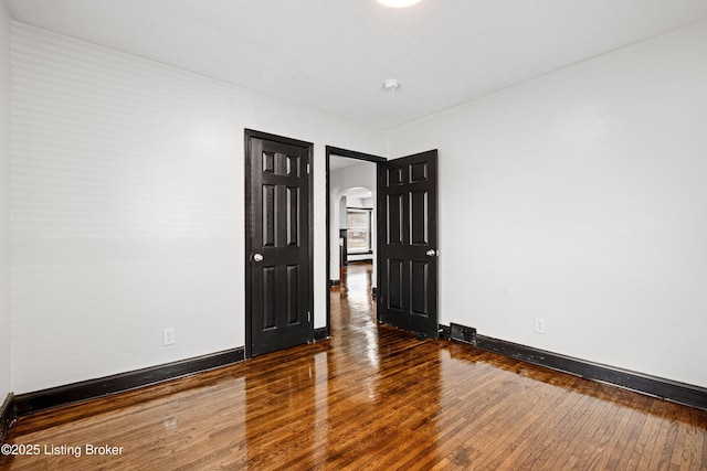 empty room with baseboards, arched walkways, and wood finished floors