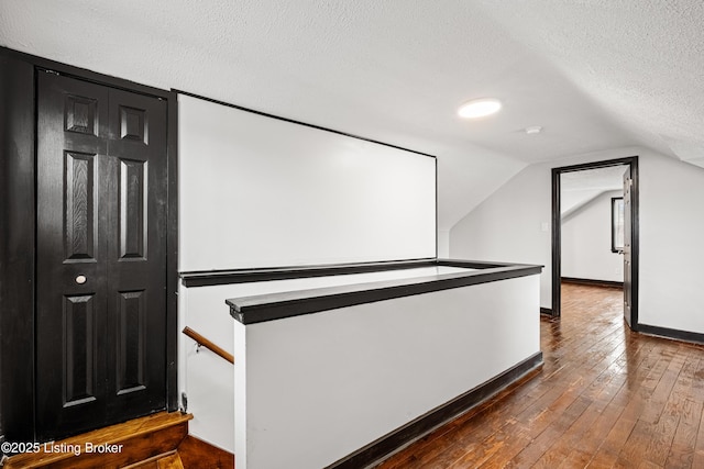 hallway with lofted ceiling, dark wood-type flooring, a textured ceiling, an upstairs landing, and baseboards