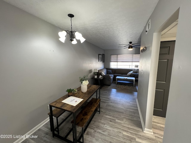 hallway featuring baseboards, a textured ceiling, an inviting chandelier, and wood finished floors