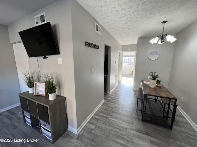 hallway featuring visible vents, an inviting chandelier, a textured ceiling, wood finished floors, and baseboards