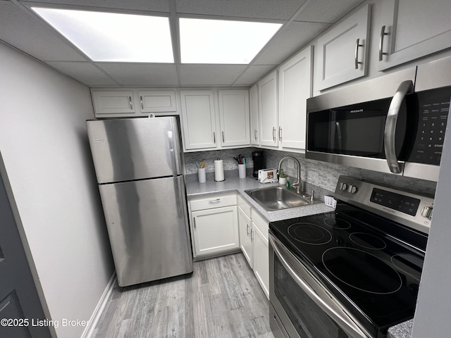 kitchen featuring stainless steel appliances, a sink, white cabinets, light countertops, and backsplash