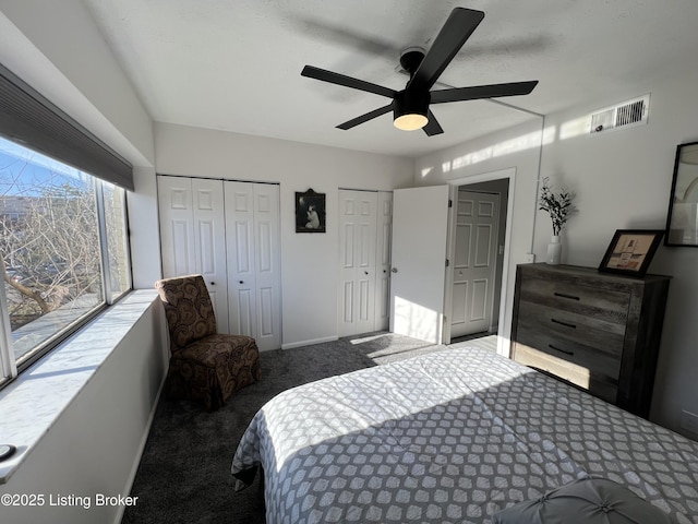 carpeted bedroom featuring baseboards, visible vents, ceiling fan, and multiple closets