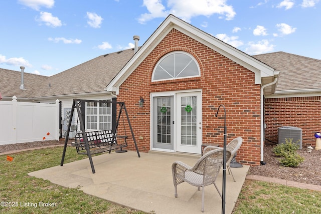 rear view of house with central AC, brick siding, a shingled roof, fence, and a patio area