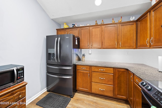 kitchen featuring appliances with stainless steel finishes, light wood-type flooring, brown cabinets, and light stone counters