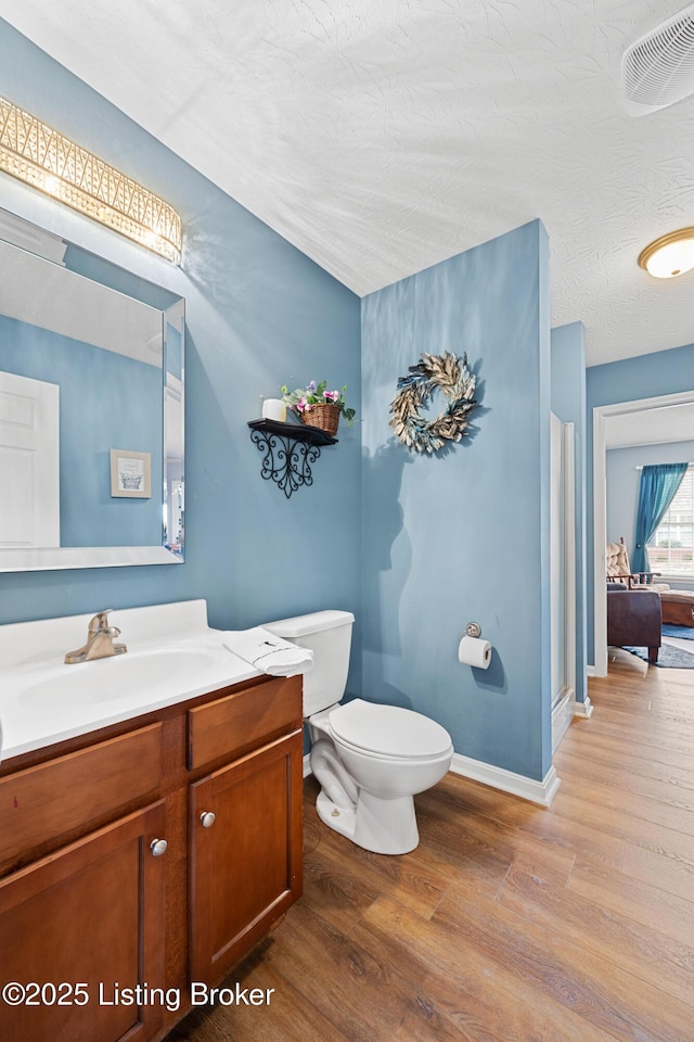 bathroom with toilet, vanity, wood finished floors, and visible vents