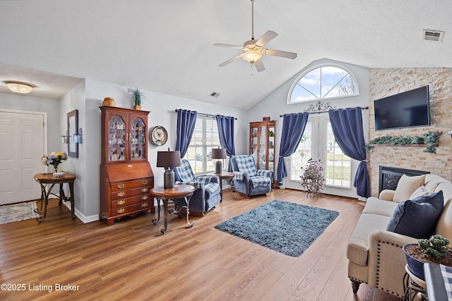 living room with a textured ceiling, visible vents, wood finished floors, and a stone fireplace