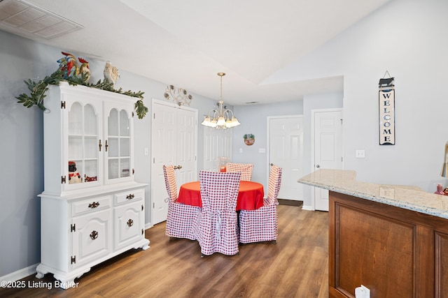 dining area with baseboards, visible vents, wood finished floors, vaulted ceiling, and a chandelier