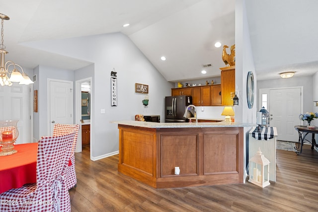 kitchen with lofted ceiling, brown cabinetry, refrigerator with ice dispenser, wood finished floors, and a peninsula