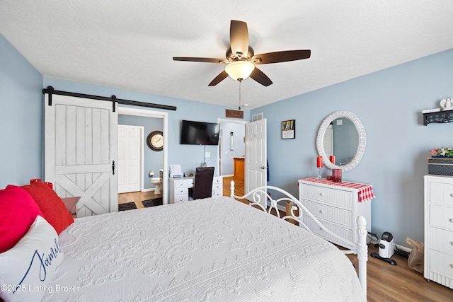 bedroom featuring visible vents, a barn door, a ceiling fan, connected bathroom, and wood finished floors