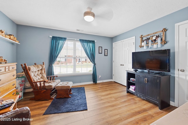 living area featuring a textured ceiling, light wood-type flooring, visible vents, and baseboards