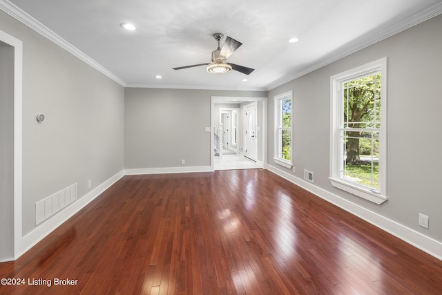 empty room with wood-type flooring, visible vents, crown molding, and baseboards