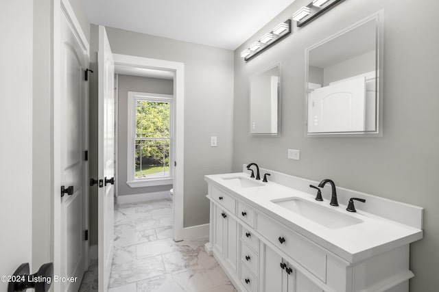 full bathroom featuring marble finish floor, double vanity, a sink, and baseboards