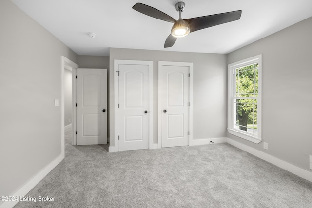 unfurnished bedroom featuring carpet floors, ceiling fan, baseboards, and two closets