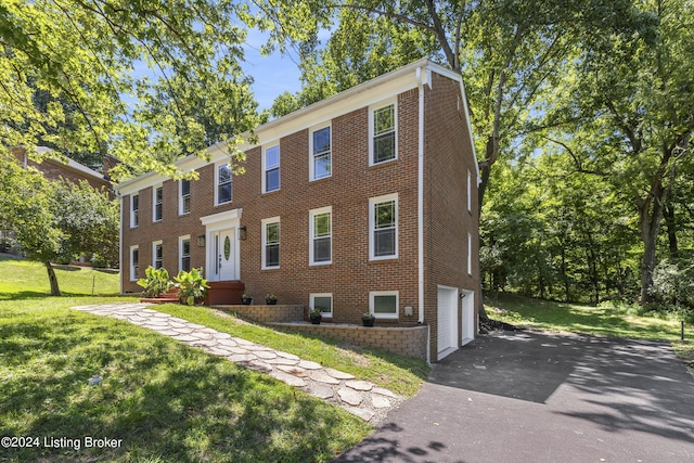 view of front facade featuring a garage, brick siding, a front yard, and aphalt driveway