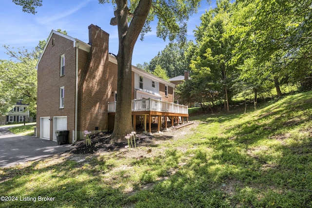 view of side of home with driveway, a chimney, an attached garage, a wooden deck, and brick siding