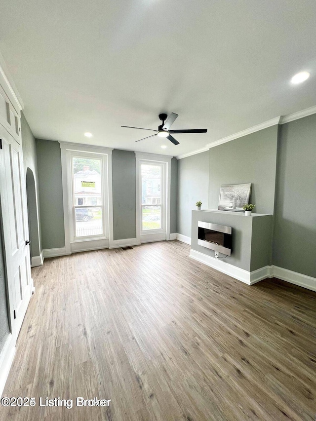 unfurnished living room with baseboards, a ceiling fan, ornamental molding, wood finished floors, and a fireplace