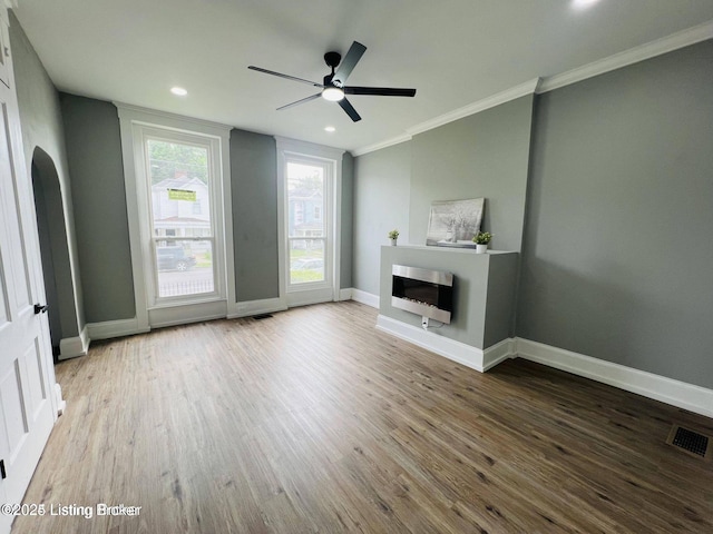 unfurnished living room featuring crown molding, a fireplace, visible vents, wood finished floors, and baseboards