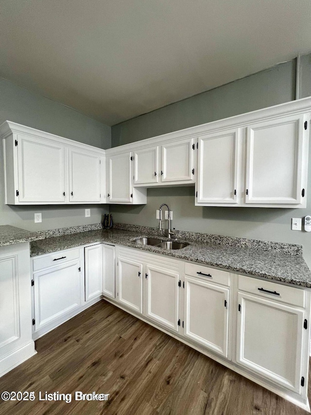 kitchen featuring dark wood-style floors, white cabinets, a sink, and light stone counters