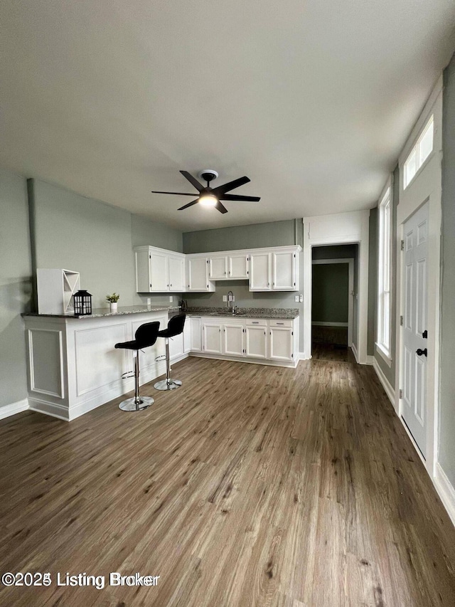 kitchen featuring baseboards, white cabinets, a ceiling fan, a breakfast bar, and dark wood-type flooring