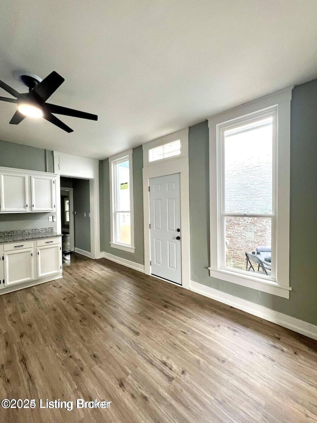 unfurnished living room featuring ceiling fan, baseboards, and wood finished floors