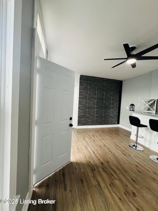 interior space with wood finished floors, a ceiling fan, and baseboards