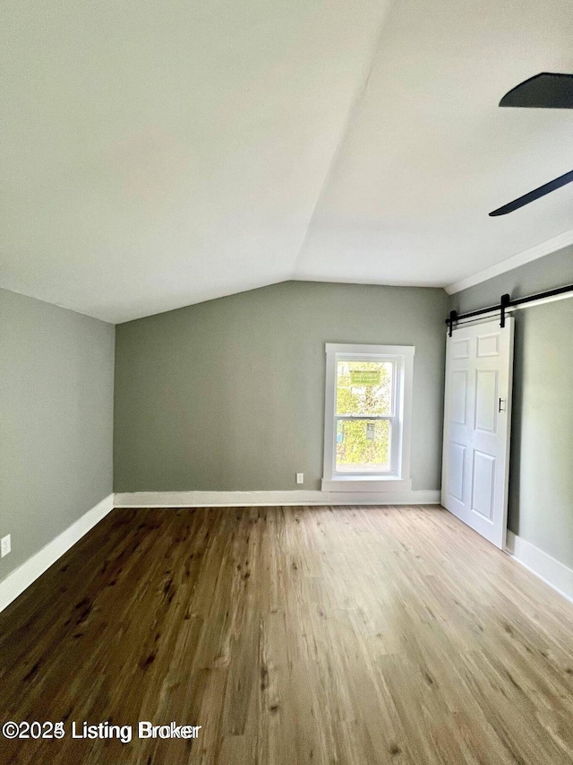 bonus room featuring wood finished floors, vaulted ceiling, baseboards, and a barn door