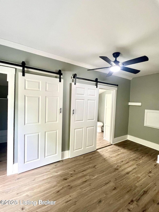 unfurnished bedroom featuring a barn door, baseboards, and wood finished floors