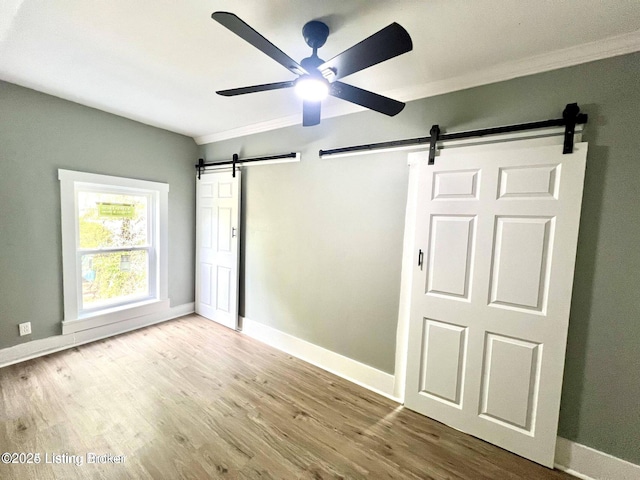 unfurnished bedroom with a barn door, wood finished floors, a ceiling fan, and baseboards