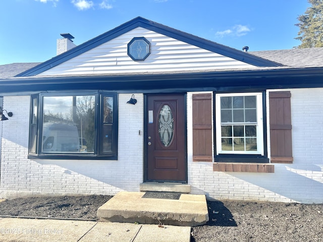 doorway to property featuring brick siding, a chimney, and a shingled roof