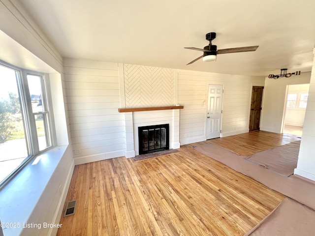 unfurnished living room with plenty of natural light, visible vents, wood finished floors, and a glass covered fireplace