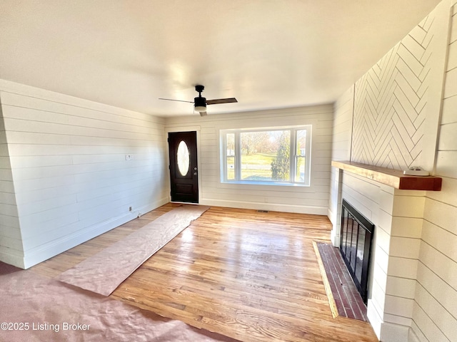 entryway featuring a ceiling fan, wood finished floors, and a glass covered fireplace