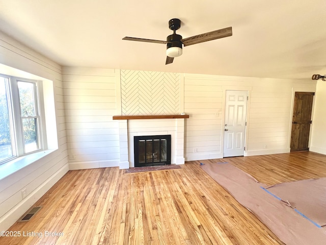 unfurnished living room featuring a glass covered fireplace, visible vents, baseboards, and wood finished floors