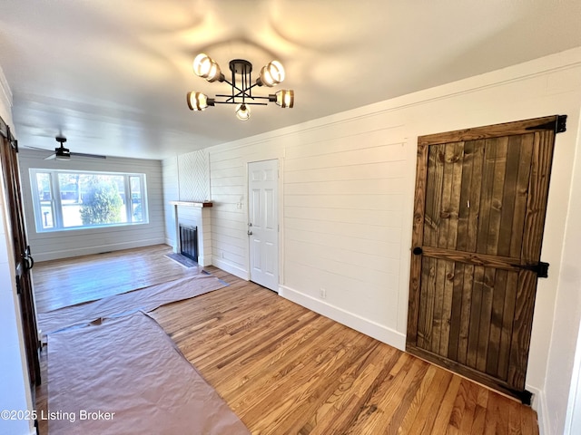 living area featuring a fireplace with flush hearth, ceiling fan with notable chandelier, baseboards, and wood finished floors