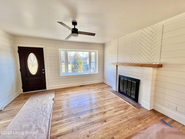 entrance foyer with a glass covered fireplace, wood finished floors, a ceiling fan, and baseboards