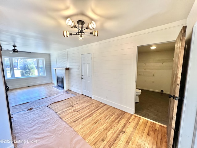 interior space featuring ceiling fan with notable chandelier, a brick fireplace, baseboards, and wood finished floors