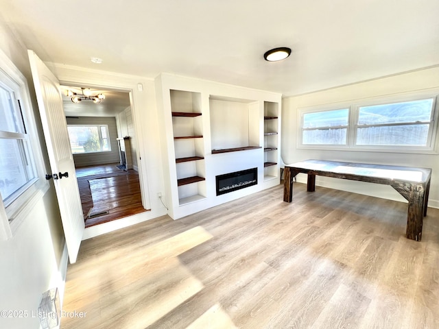 living area featuring a chandelier, light wood-type flooring, a glass covered fireplace, and built in features