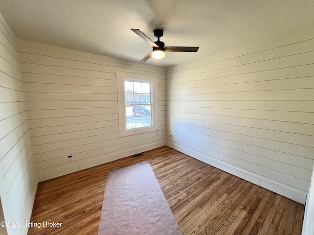 unfurnished room featuring wood walls, visible vents, a ceiling fan, and wood finished floors