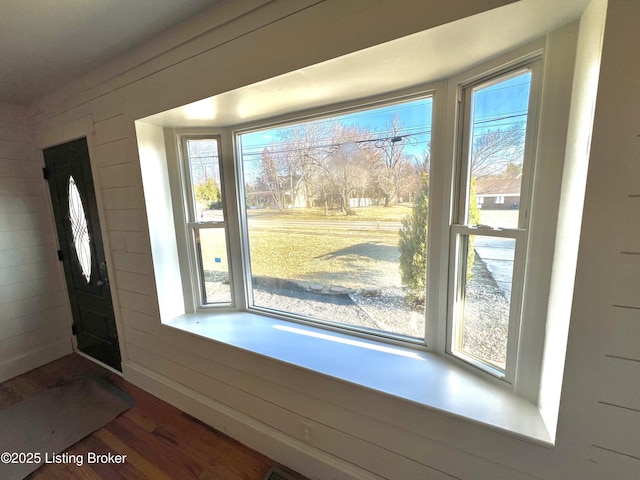 doorway with baseboards, wood finished floors, a wealth of natural light, and wooden walls