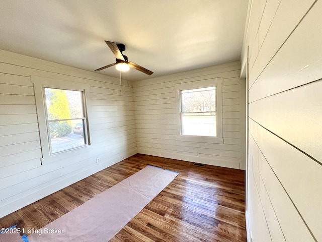 unfurnished room featuring ceiling fan, wood finished floors, visible vents, and wooden walls