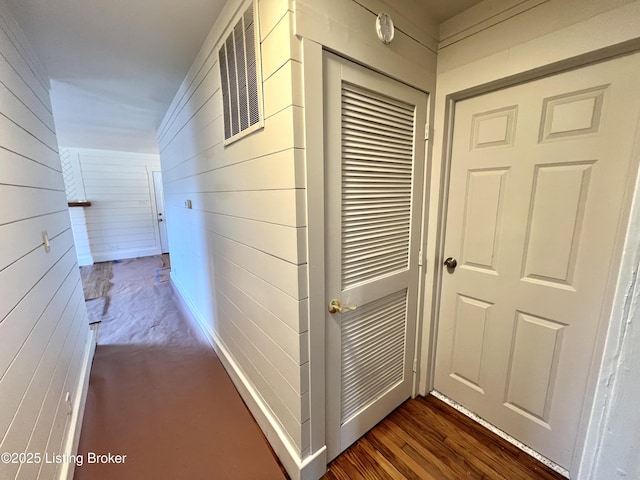 hallway featuring dark wood-style floors, wooden walls, and visible vents