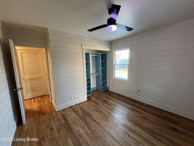 unfurnished bedroom with baseboards, visible vents, wood finished floors, wood walls, and a closet